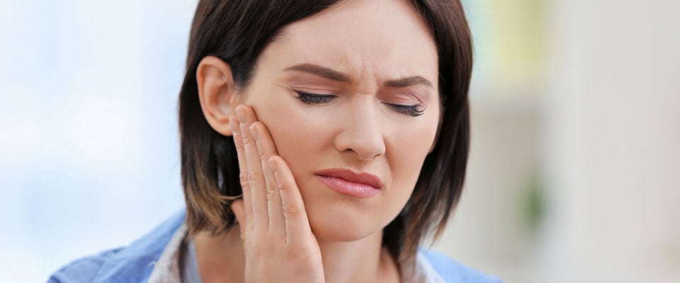 The woman experiencing tooth pain in the root canal put her hand on a cheek.